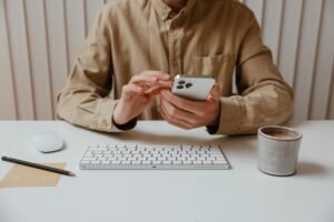 Person using smartphone at a tidy office desk with coffee, keyboard, and mouse.